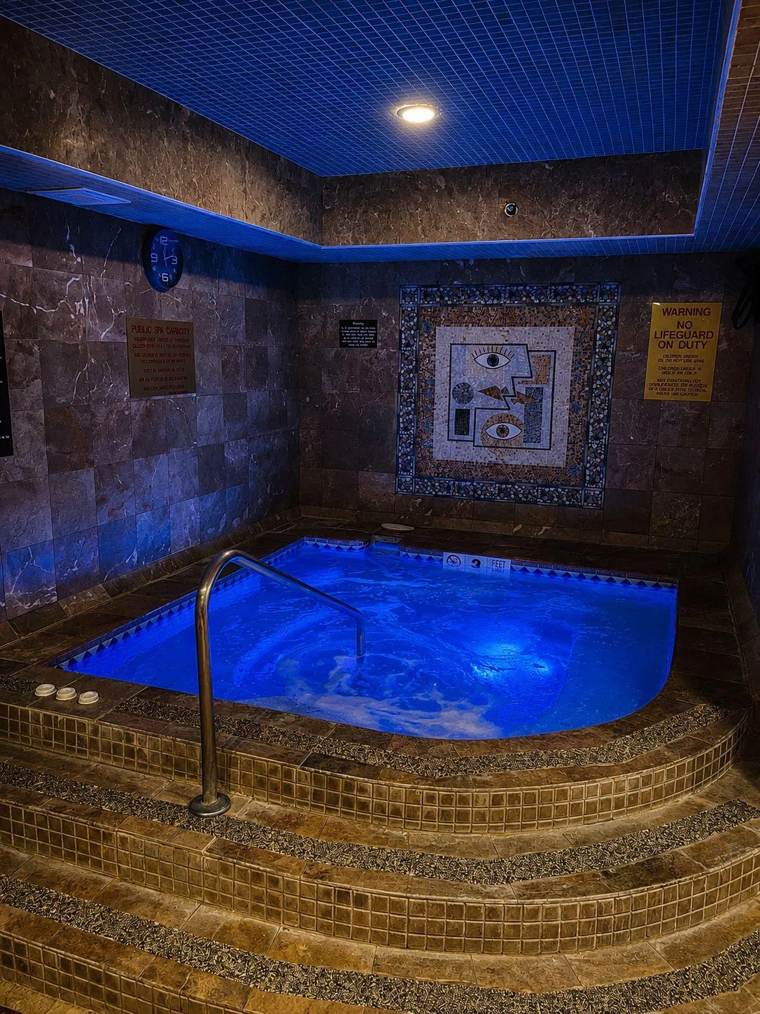 BRC's jacuzzi lit blue, tiled steps up to it and a mosaic panel on the stone wall.