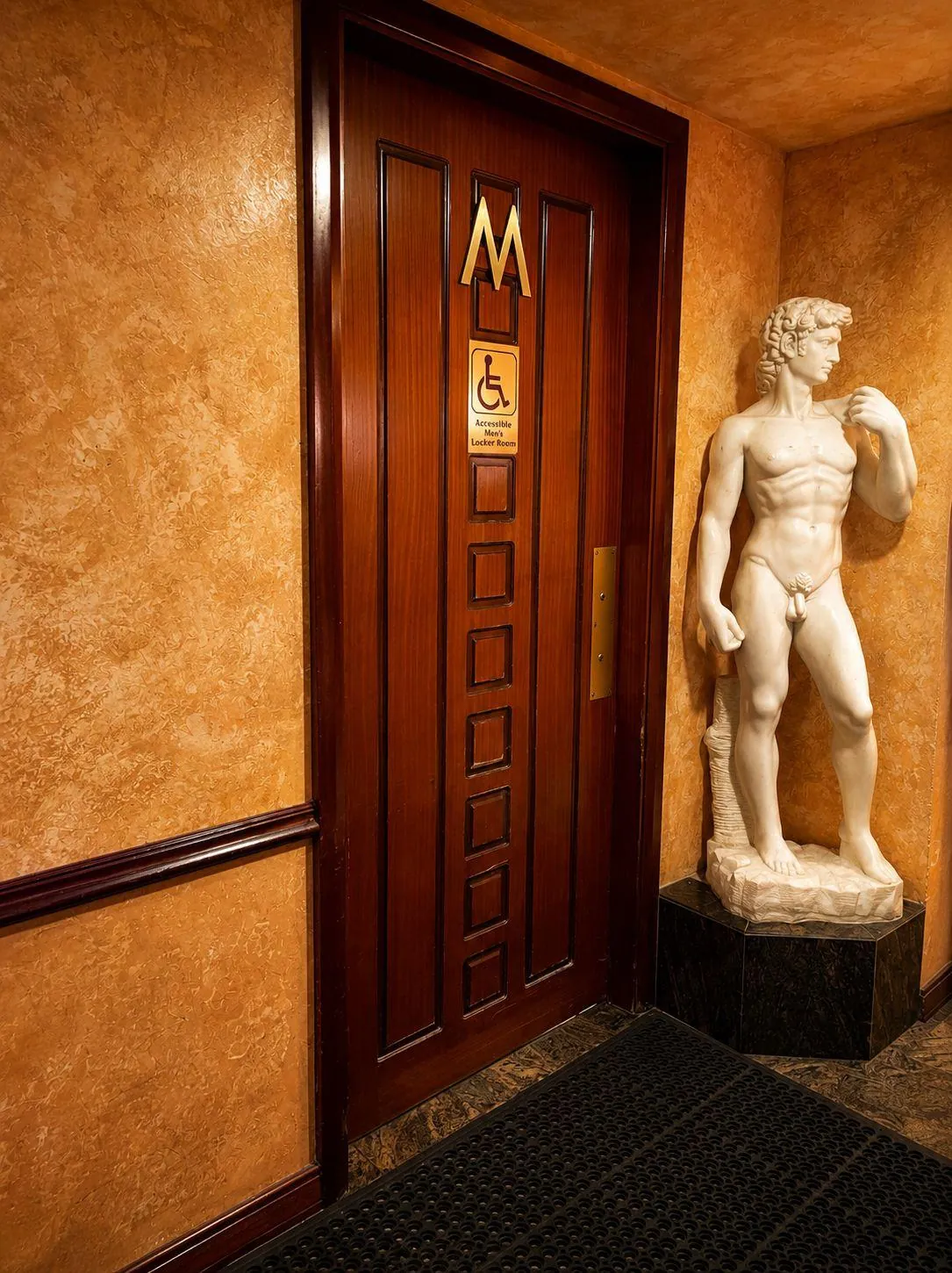 A marble statue beside the carved wooden door of the men's locker room.