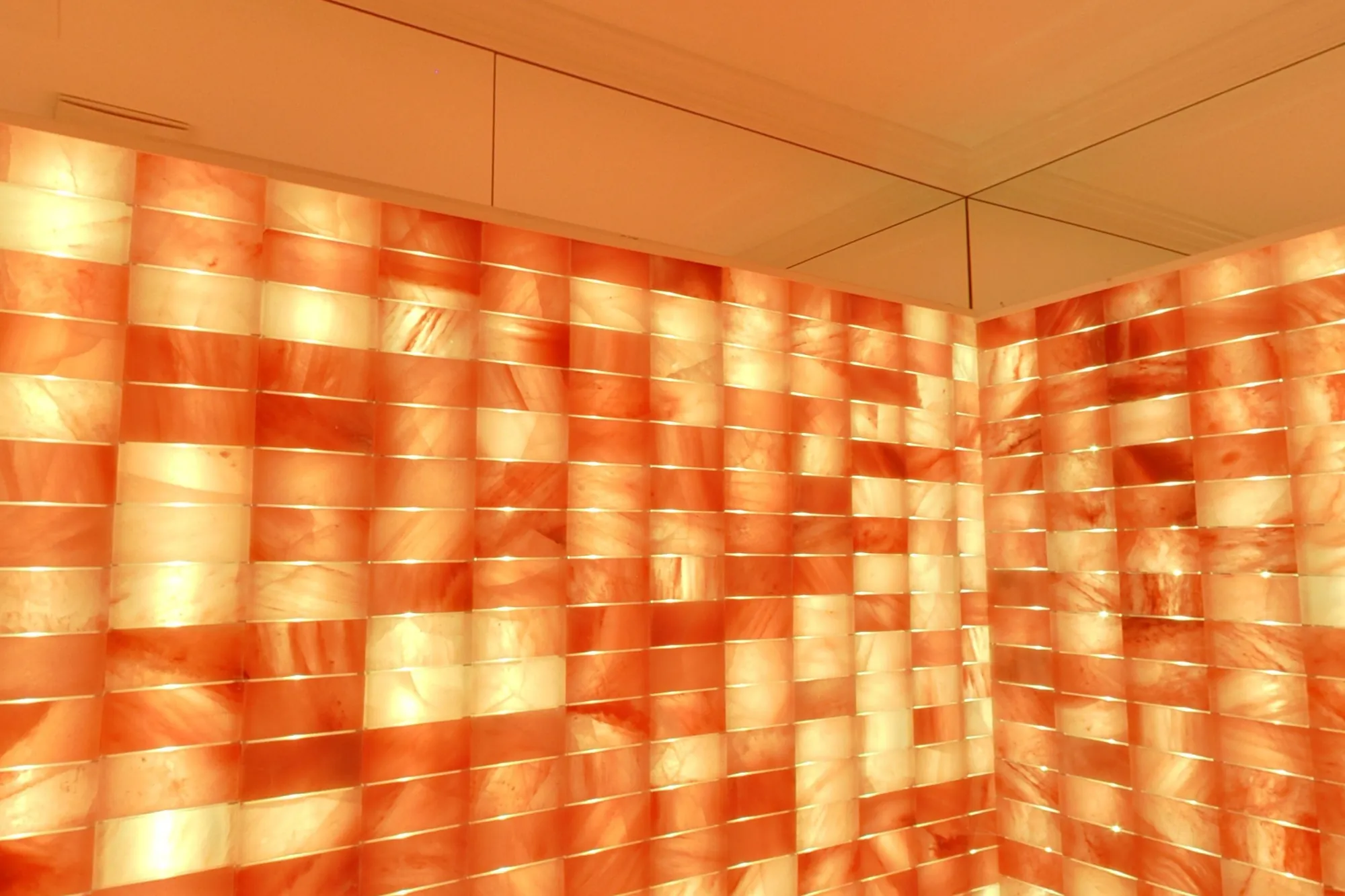 Walls of backlit Himalayan salt brick, glowing amber and rose, with a lounger in the corner.